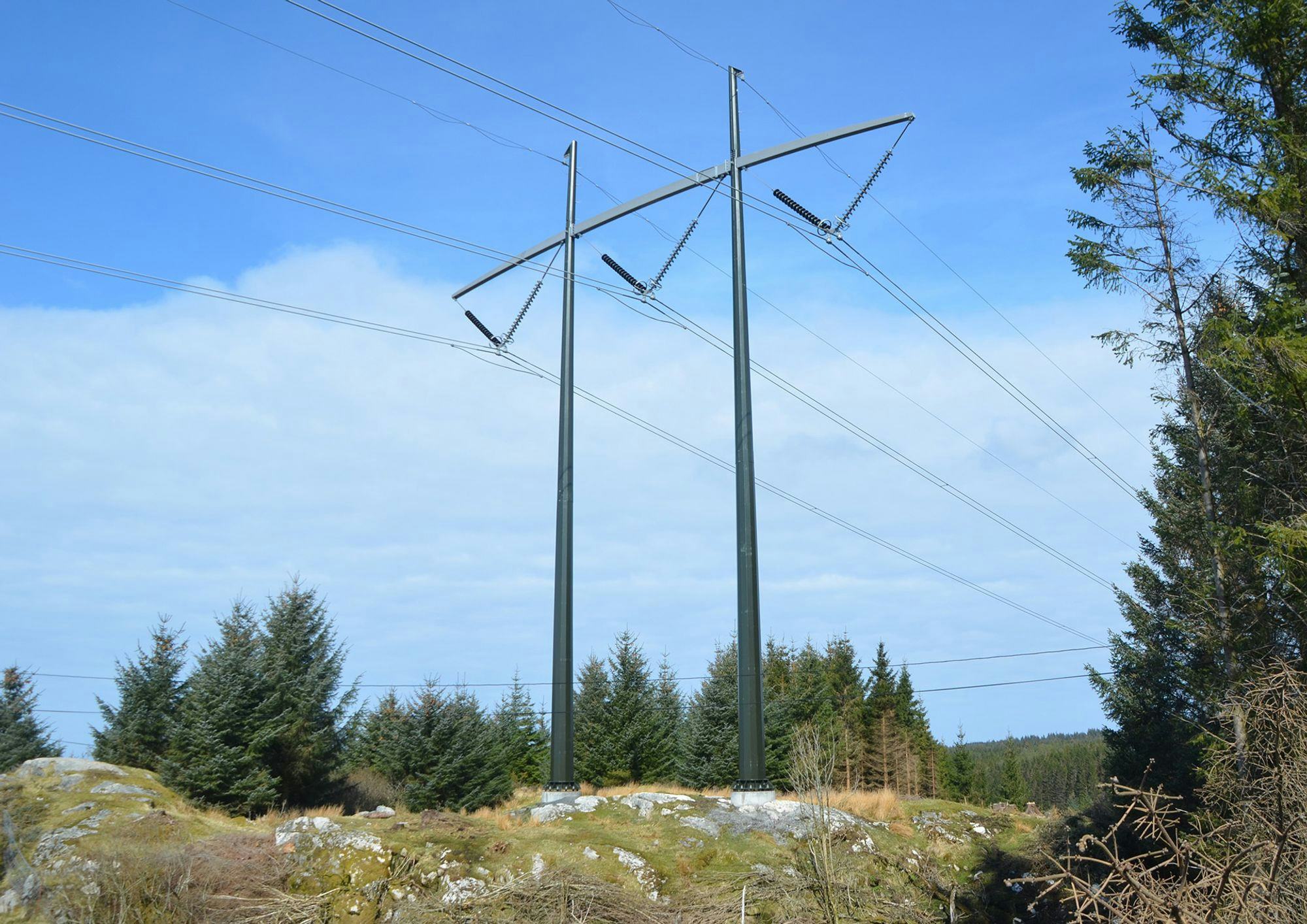 A transmission tower with cloudy blue sky and pine trees in the background