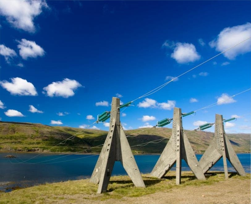 Three concrete transmissions stands before a blue lake with a cloudy blue sky in the background