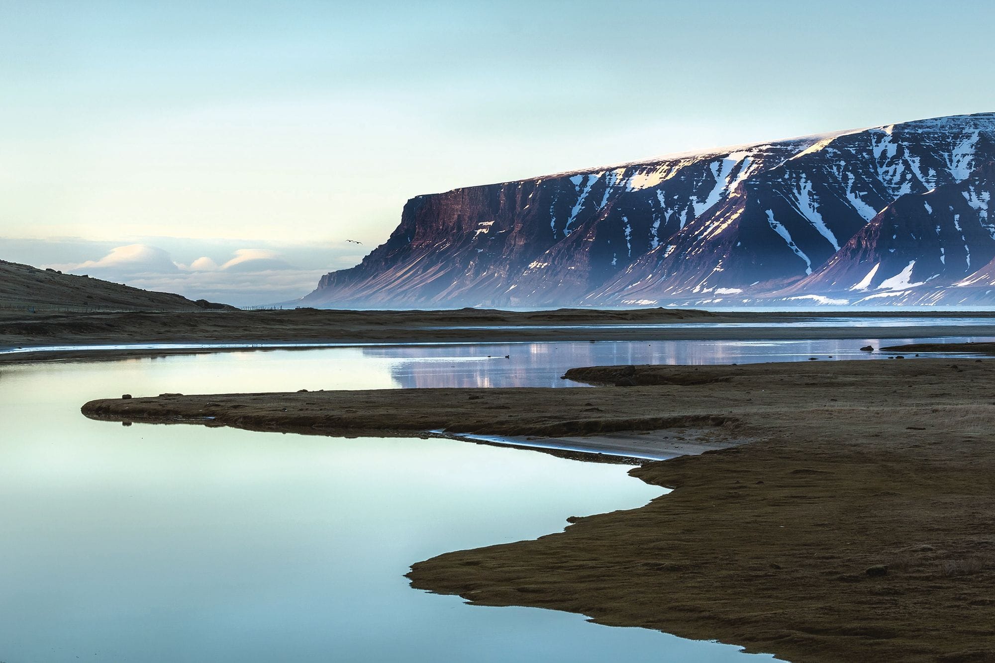 Landscape, mirror-smooth water where the land lies in headlands out onto the lake. Mountain with snow patches in the background, calm weather