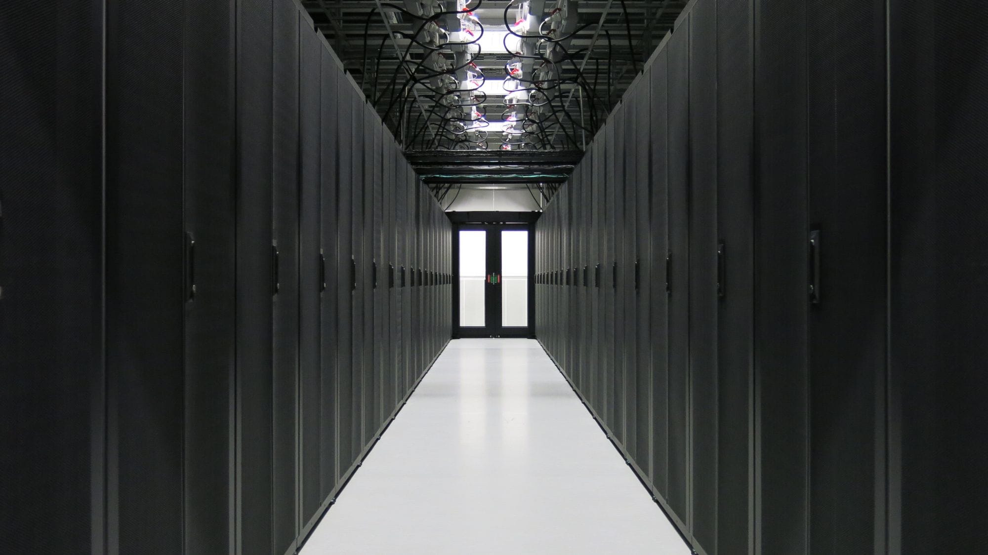 A long corridor with black cupboards on both sides, a front door at the end of the corridor. Cables from the black cabinets connected to a wire structure in the ceiling