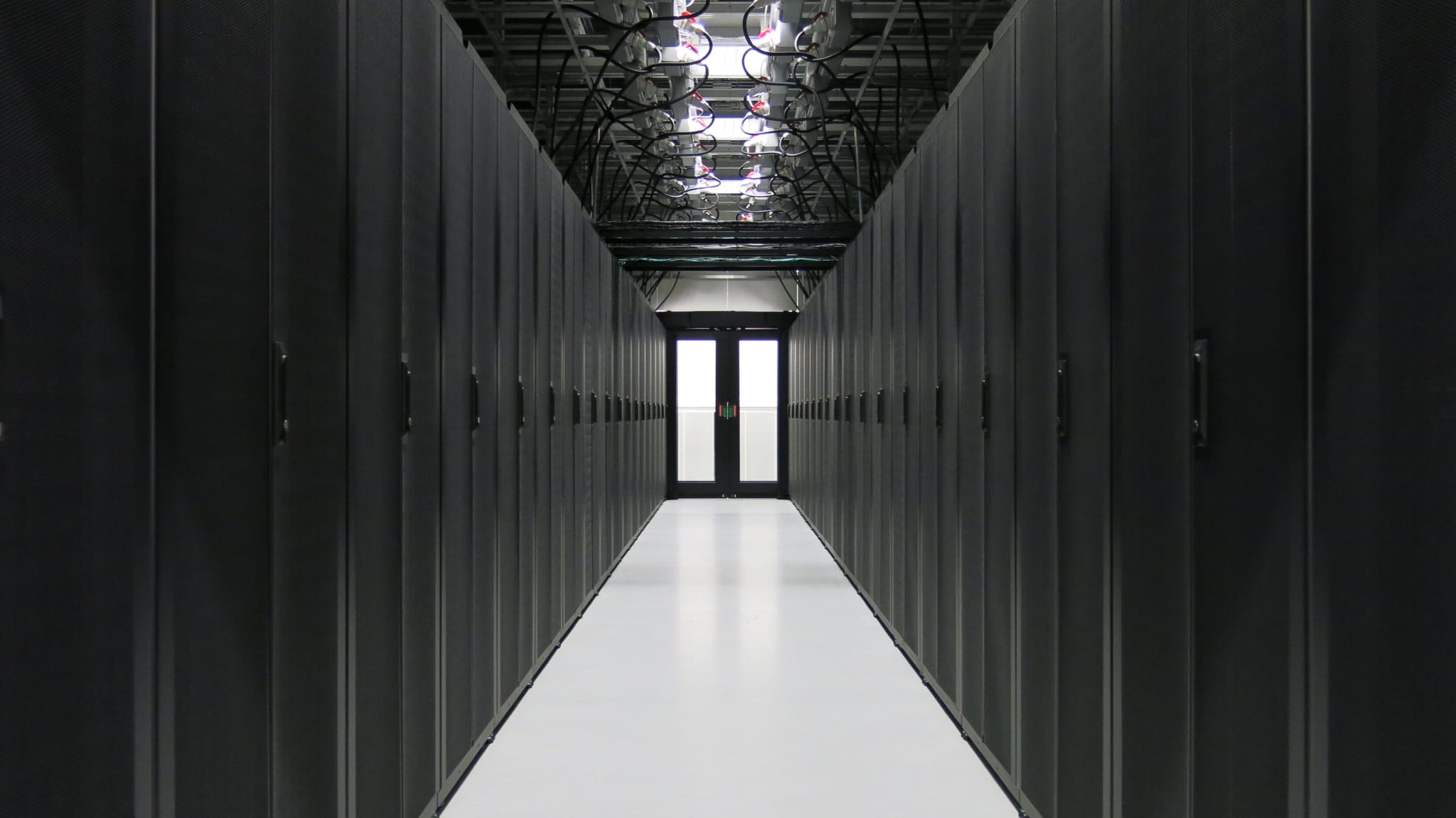 A long corridor with black cupboards on both sides, a front door at the end of the corridor. Cables from the black cabinets connected to a wire structure in the ceiling