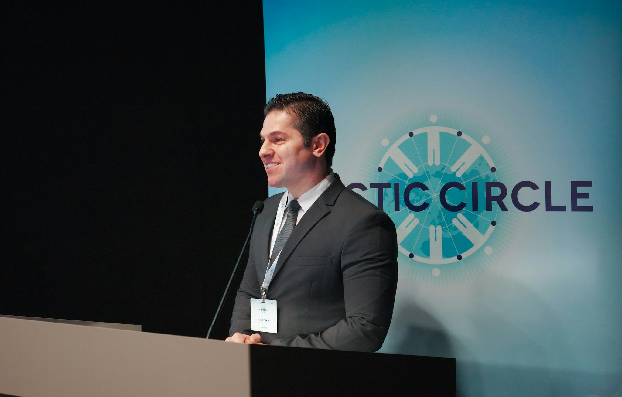 A man standing in front of a blue screen that says 'Arctic Circle' giving a speach, smiling